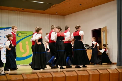 Kinder in Bregenzerwälder Tracht ziehen tanzend über die Bühne, dahinter das Banner der Landjugend Vorarlberg
