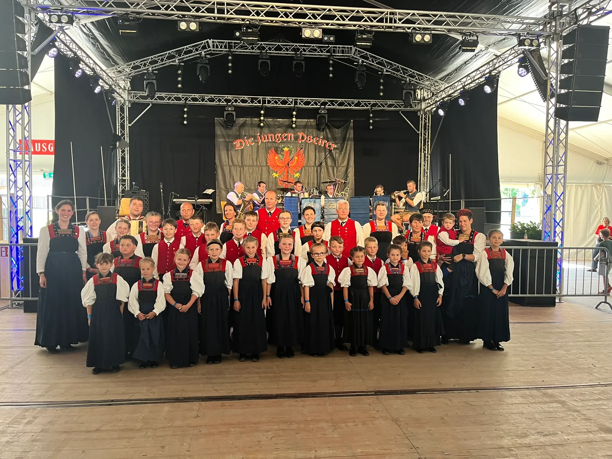 Die Kindertrachtengruppe und die Tanzgruppe Hittisau auf der Festbühne in Bezau, dahinter eine Musikkapelle