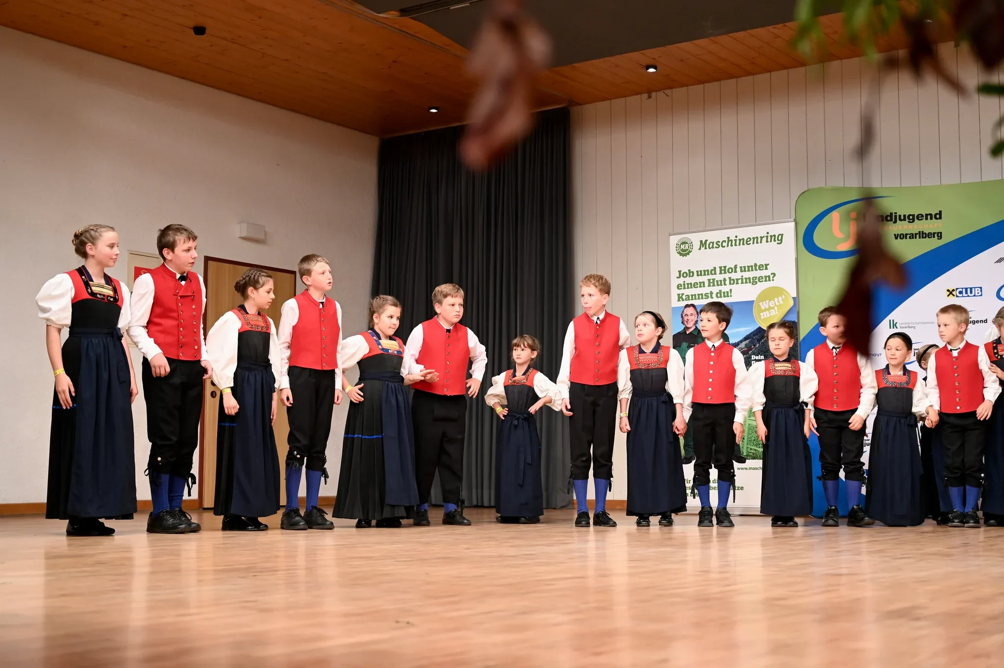 Die Kindertrachtengruppe Hittisau steht in einer Reihe auf der Bühne im Dorfsaal Alberschwende