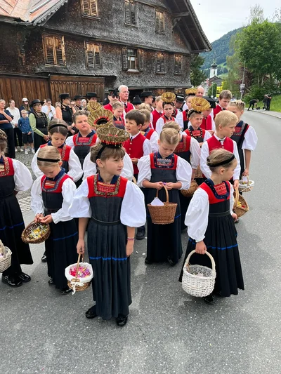 Kinder in Tracht warten mit Blumenkörbchen am Straßenrand auf den Beginn der Prozession