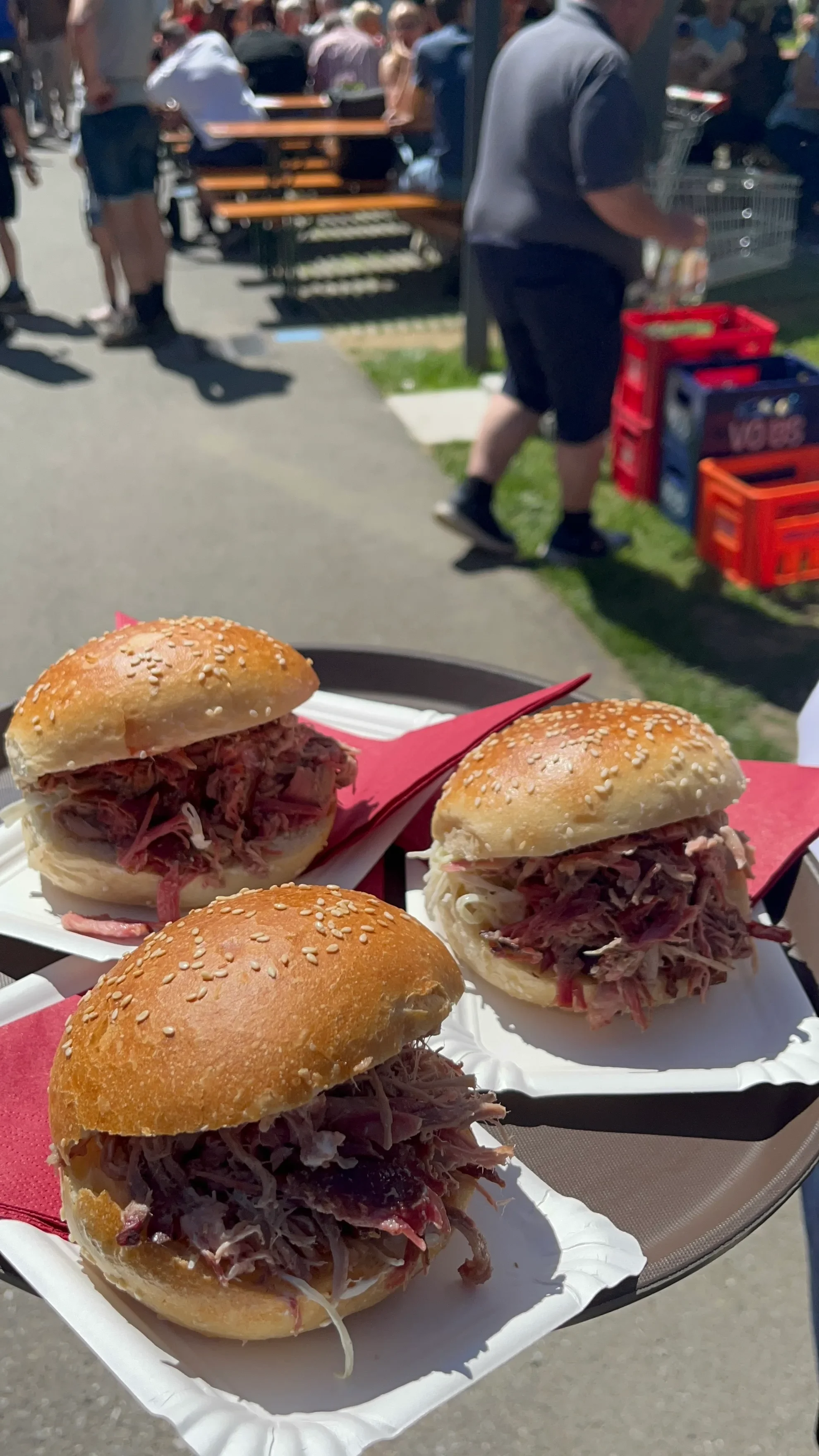 Drei Pulled-Pork-Burger auf Papptellern, im Hintergrund die Bierbänke des Wäldermarkts