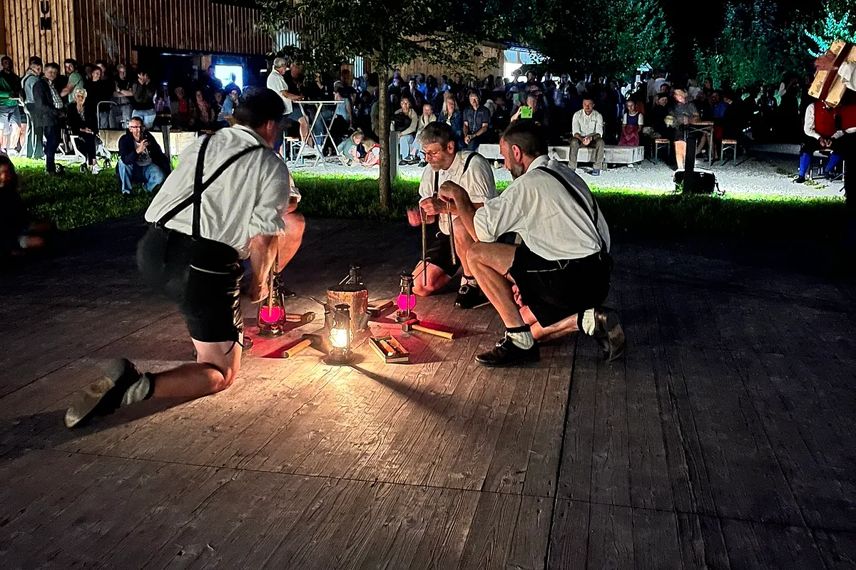 Drei Schuhplattler bei einem Abendauftritt auf einer Bühne im Freien